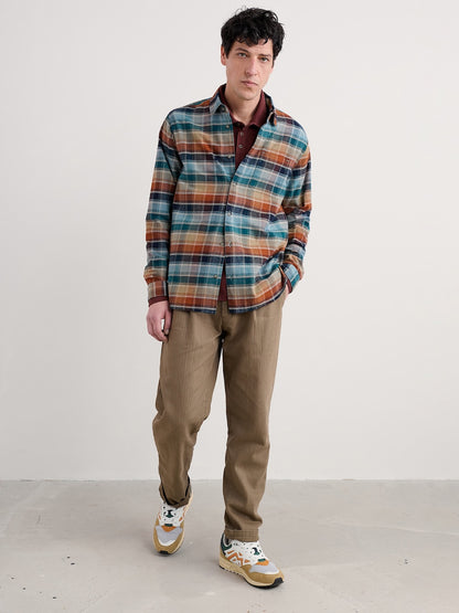 Man wearing a plaid shirt and brown pants against a white background