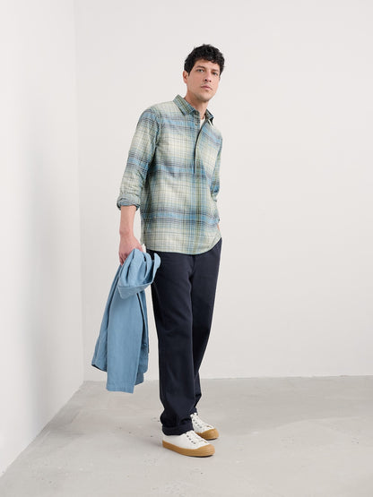 Man wearing a plaid shirt and dark pants holding a blue jacket against a white background