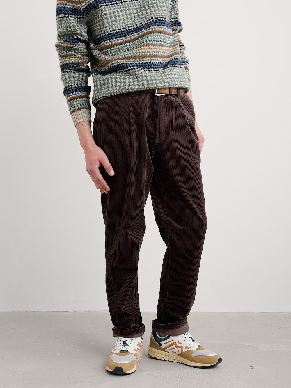 Person wearing a patterned sweater and brown pants on a plain background