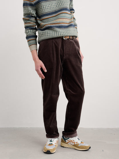 Person wearing a patterned sweater and brown pants on a plain background
