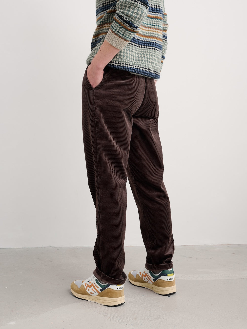 Person wearing brown pants and a patterned sweater against a white background