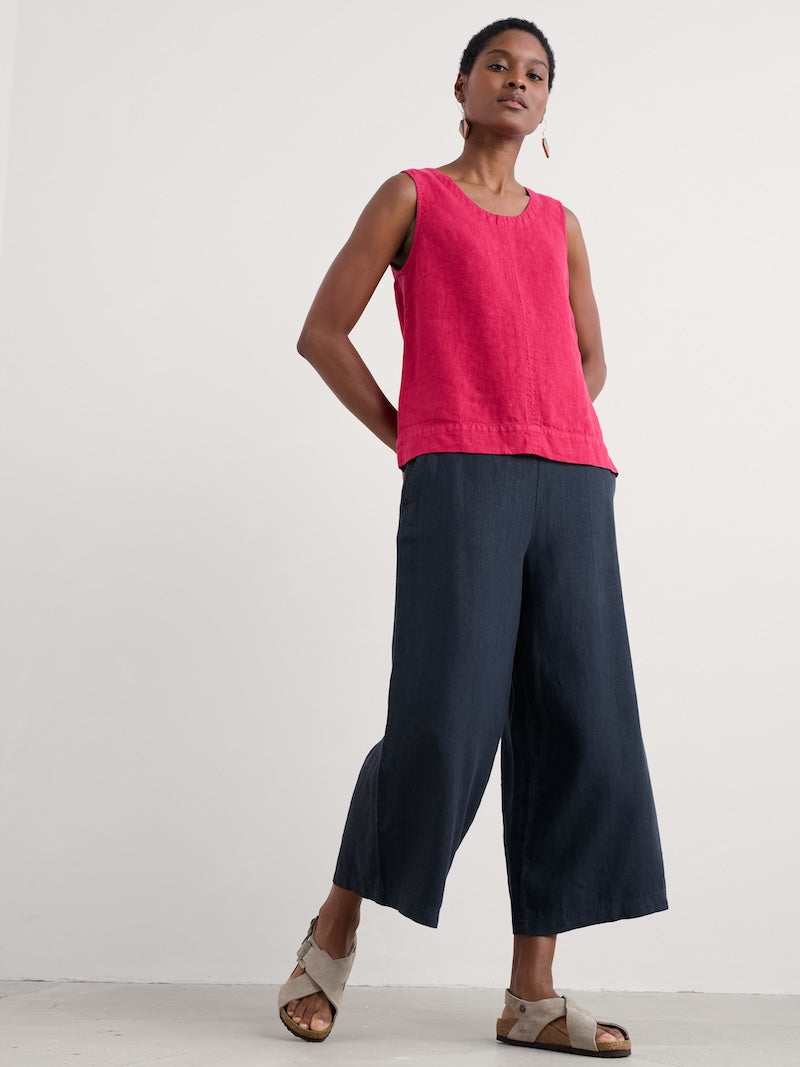 Woman wearing a pink sleeveless top and navy wide-leg pants on a white background