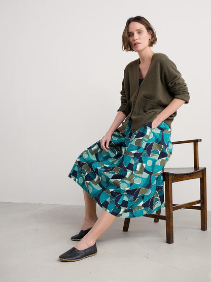 Woman sitting on a chair wearing a green cardigan and patterned skirt.