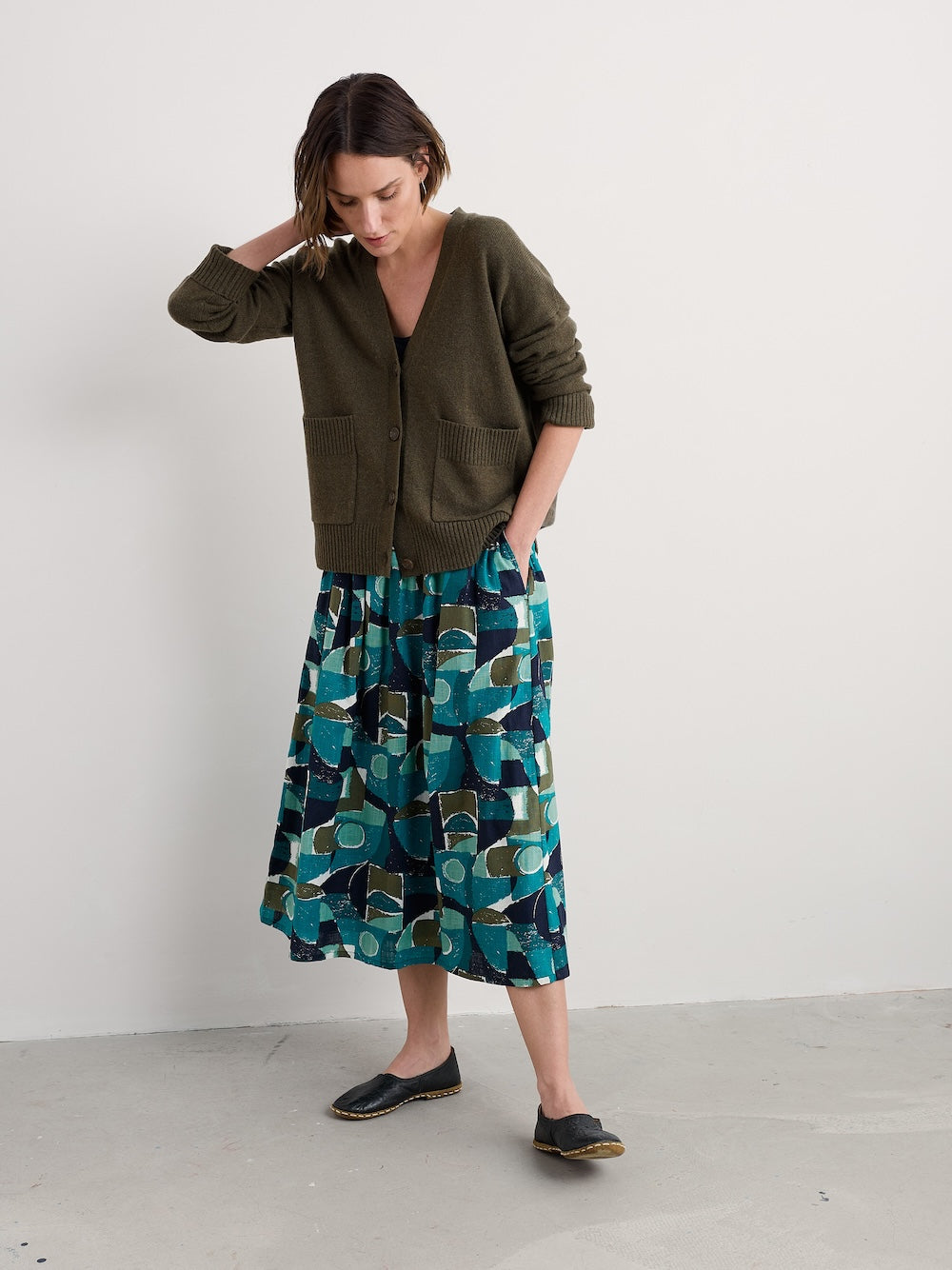 Woman wearing a green cardigan and patterned skirt on a white background