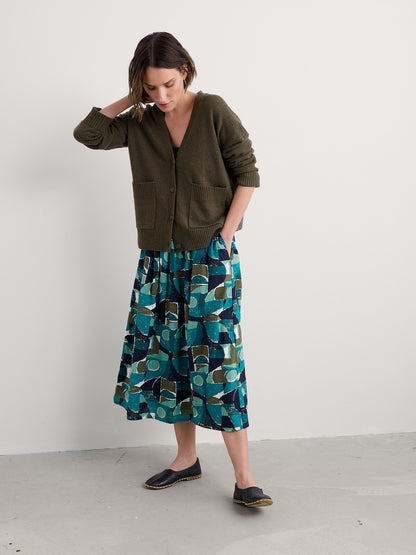 Woman wearing a green cardigan and patterned skirt on a white background