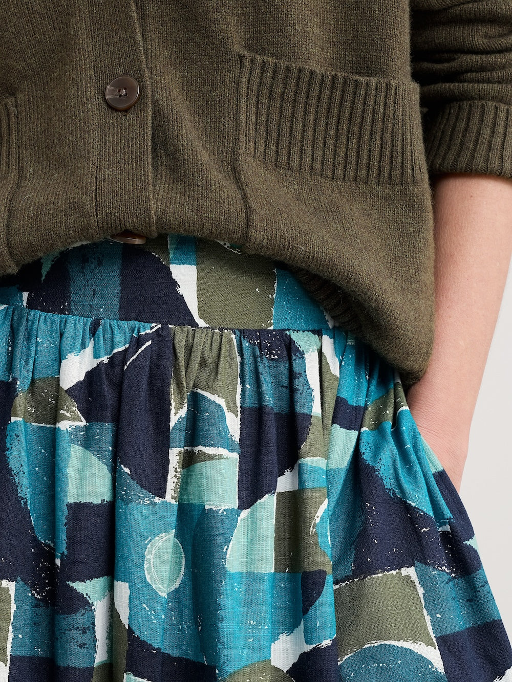 Person wearing a green cardigan and a patterned skirt with abstract designs.