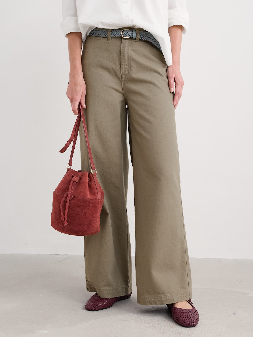 Person wearing beige wide-leg pants and holding a red handbag on a plain background