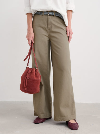 Person wearing beige wide-leg pants and holding a red handbag on a plain background