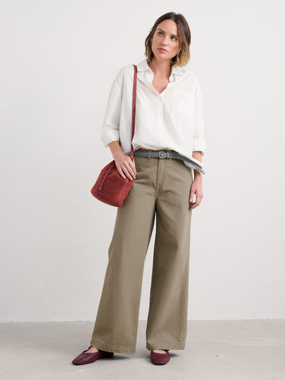 Woman wearing a white blouse and beige wide-leg pants with a red bag on a white background