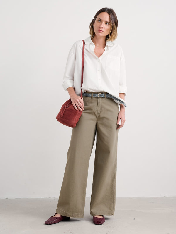 Woman wearing a white blouse and beige wide-leg pants with a red bag on a white background
