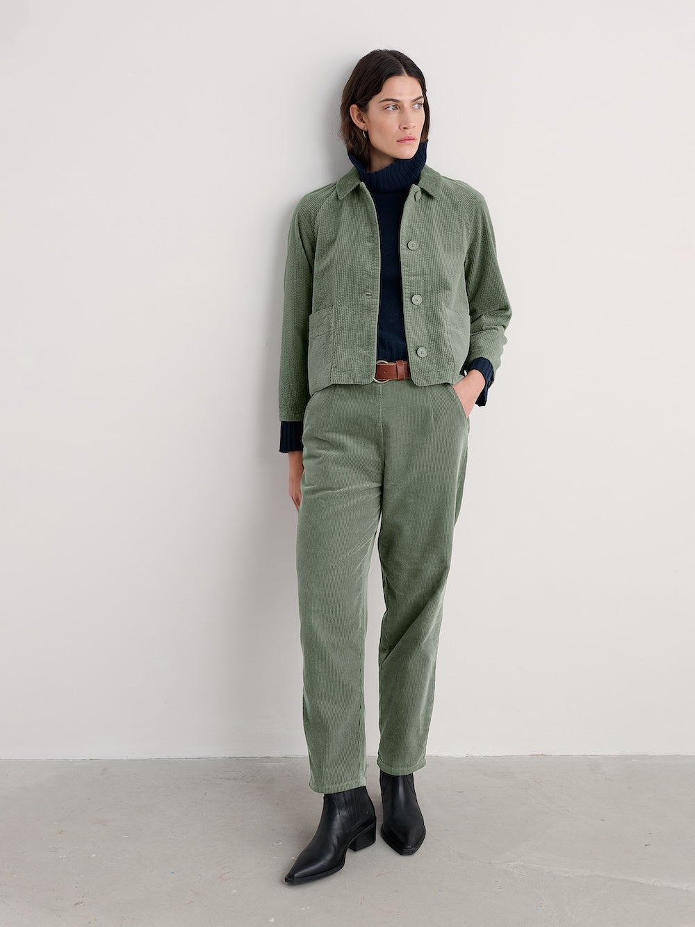 Person wearing a green jacket and pants with a white background