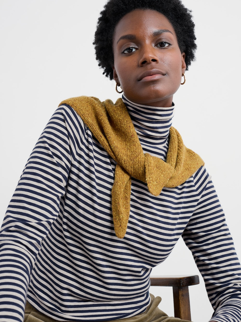 Person wearing a mustard yellow scarf over a striped shirt against a white background