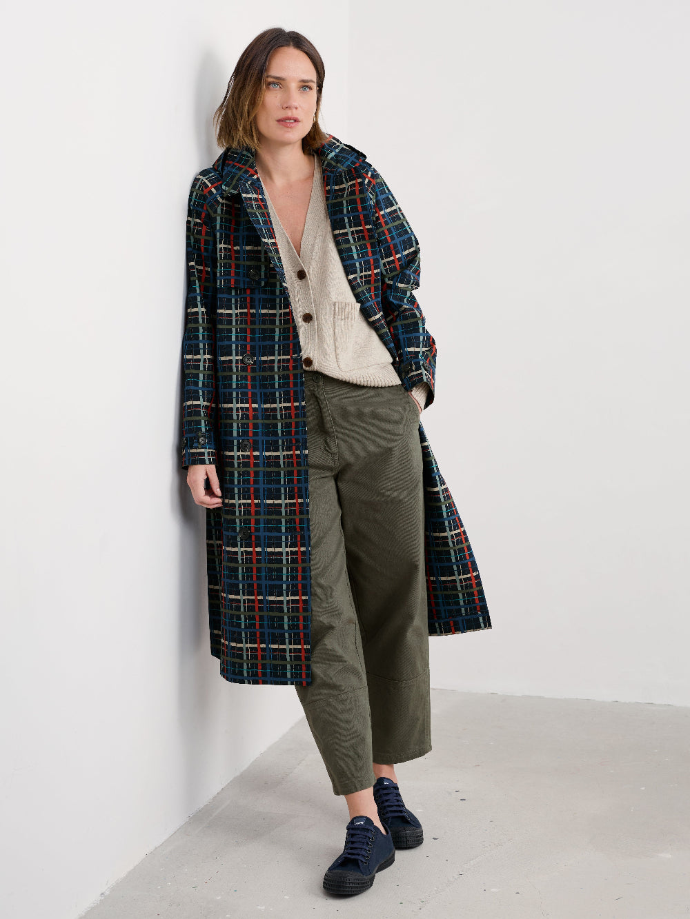 Woman wearing a plaid rain coat and green pants against a white background
