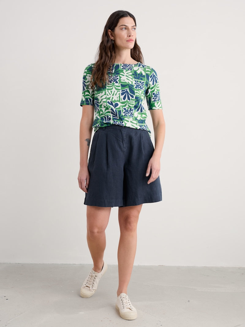 Woman wearing a patterned top and navy skirt on a white background