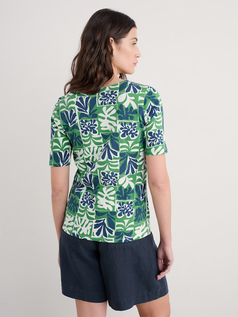 Woman wearing a green and blue patterned top with navy shorts on a plain background