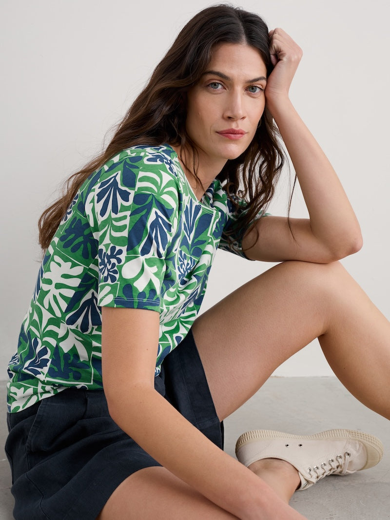 Woman wearing a green and blue leaf-patterned shirt sitting on the floor.