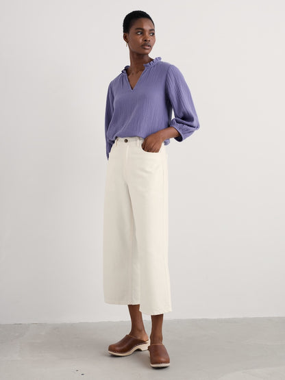 Woman wearing a purple blouse and white pants against a white background