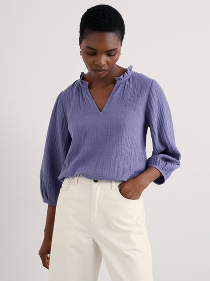 Woman wearing a purple blouse and white pants against a plain background
