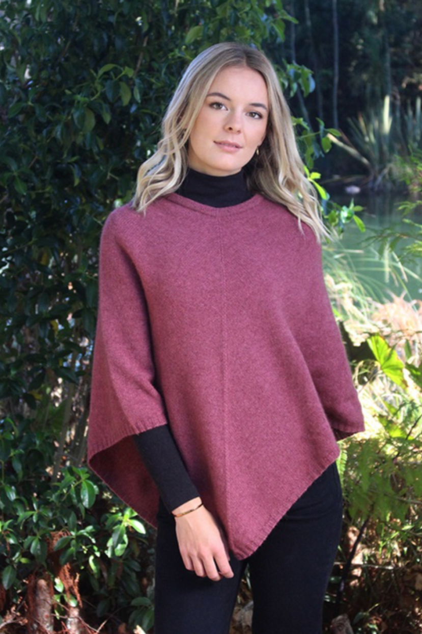 Orchid  pink possum and merino wool poncho on female model standing in garden. Warm, soft, lightweight possum and merino wool. Lothlorian