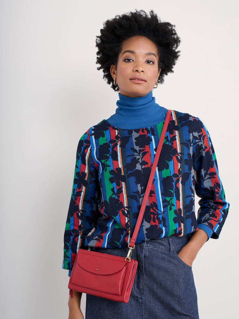 Woman wearing a colorful patterned shirt with a red bag against a white background