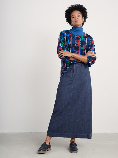 Woman wearing a colourful patterned shirt and denim skirt against a white background