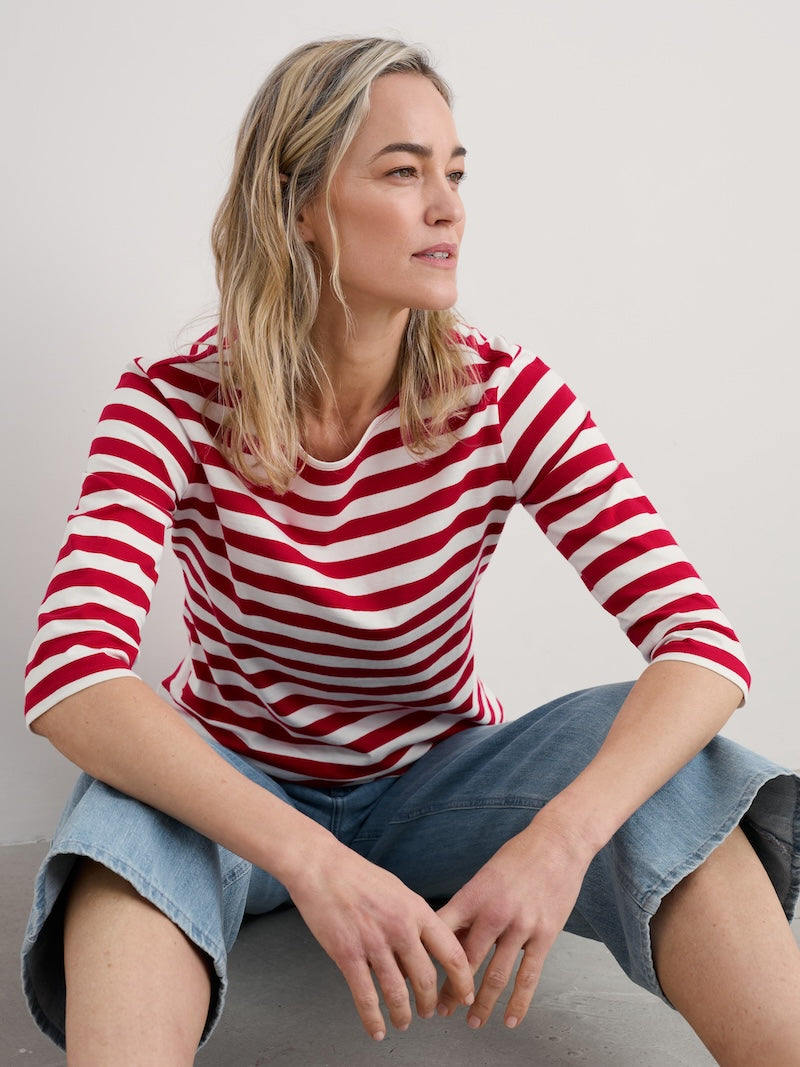 Woman wearing a red and white striped shirt sitting on a gray surface.