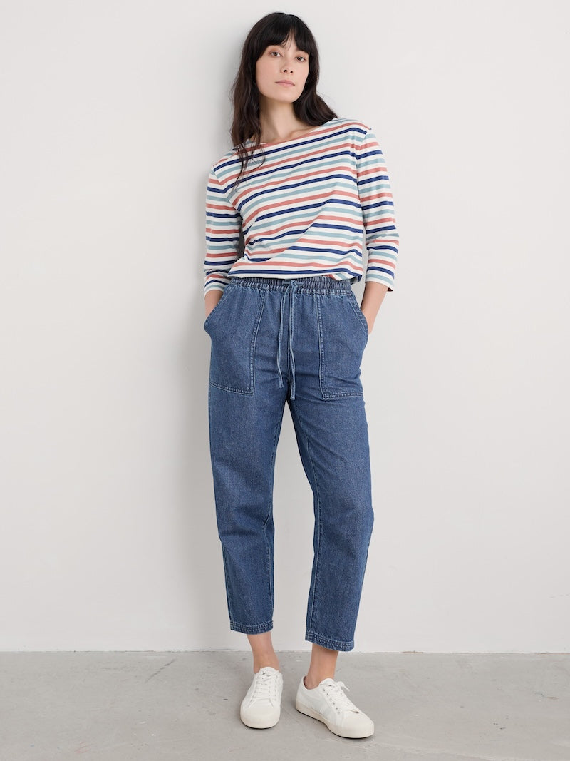 Woman wearing a striped long sleeve top and blue jeans against a white background