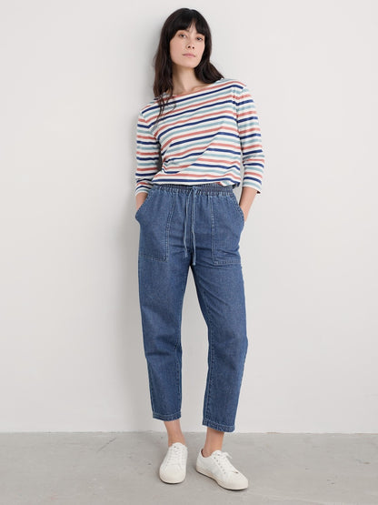 Woman wearing a striped long sleeve top and blue jeans against a white background