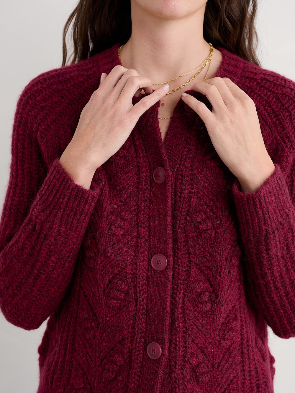Person wearing a burgundy knitted cardigan with a plain background
