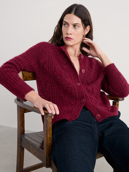 Woman wearing a burgundy cardigan sitting on a wooden chair against a white background