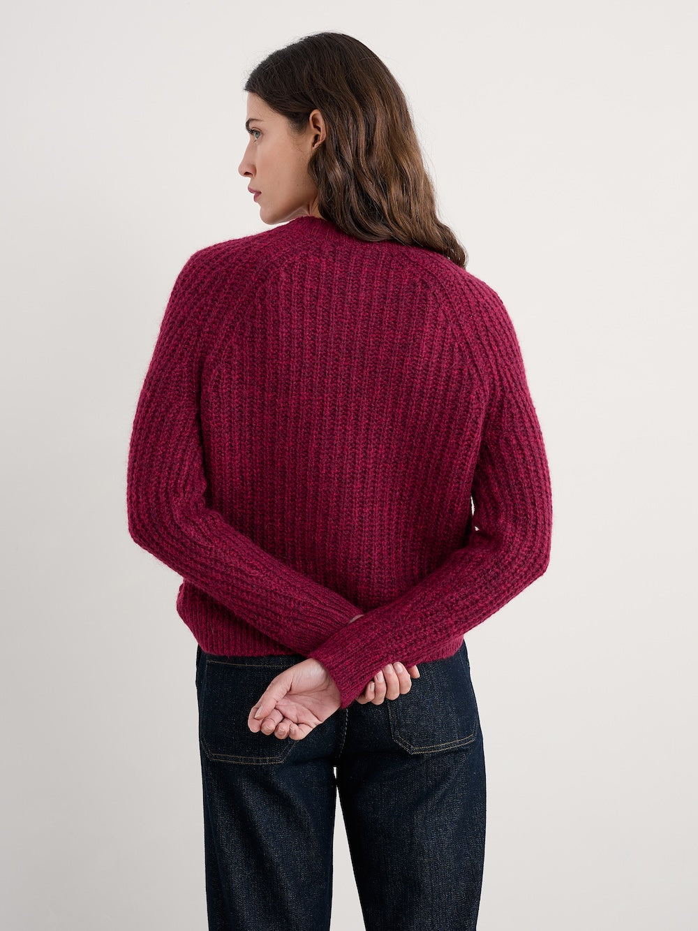 Person wearing a maroon cardigan and dark jeans on a plain background
