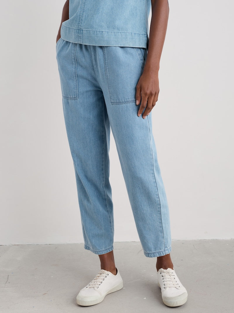 Woman wearing light blue jeans and white sneakers on a plain background