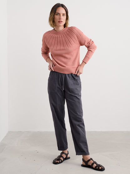 Woman wearing a pink sweater and dark pants against a white background