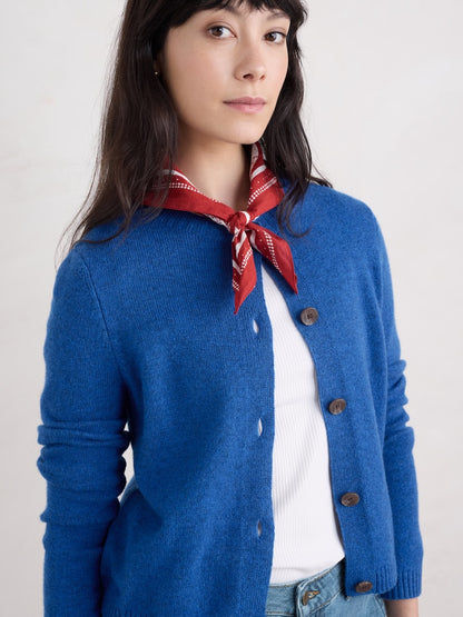 Woman wearing a blue cardigan with a red scarf and white shirt on a plain background