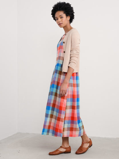 Woman wearing a colorful plaid dress with a beige cardigan on a white background