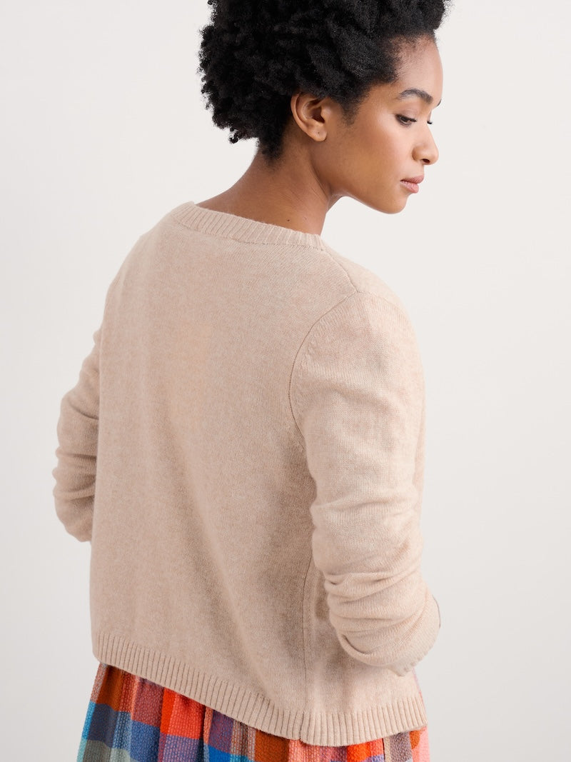 Woman wearing a beige sweater over a colorful dress on a white background