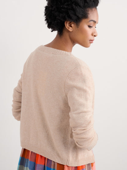 Woman wearing a beige sweater over a colorful dress on a white background