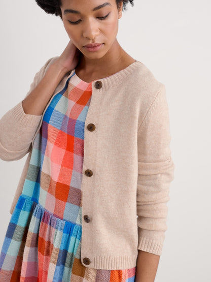 Woman wearing a beige cardigan over a colorful plaid dress on a white background
