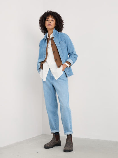 Person wearing a denim jacket, white shirt, and light blue jeans on a plain background