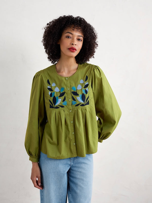 Woman wearing a green blouse with floral embroidery on a white background