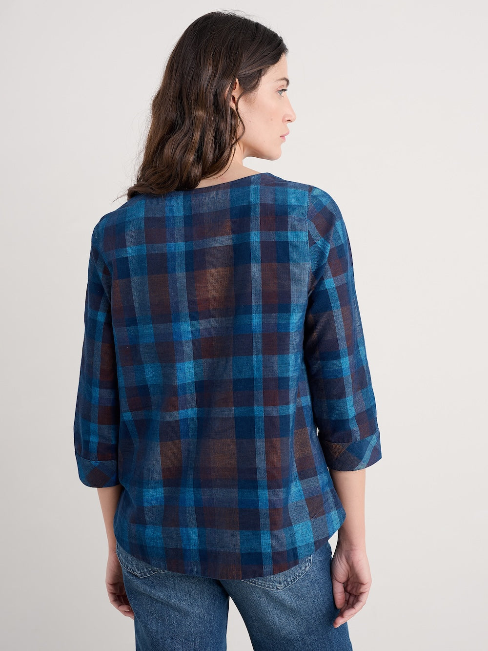 Woman wearing a blue plaid shirt and jeans on a plain background