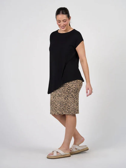 Woman wearing a black bamboo asymmetrical top and leopard print skirt on a white background.