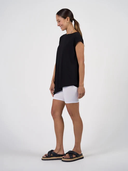 Woman wearing a black asymmetrical top and white shorts on a white background.