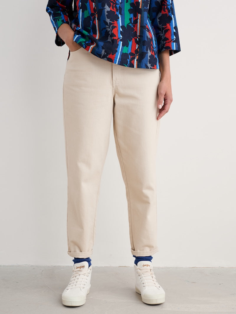 Woman  wearing a colorful top, beige pants, and white sneakers on a plain background