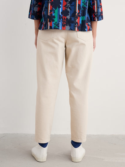 Woman wearing a colourful floral blouse and beige jeans on a plain background