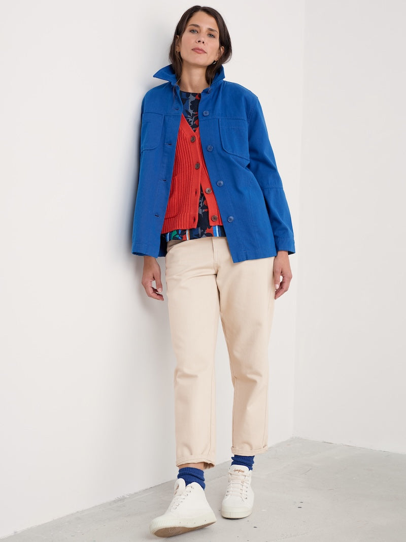 Woman wearing a blue jacket, red shirt, and beige pants against a white background