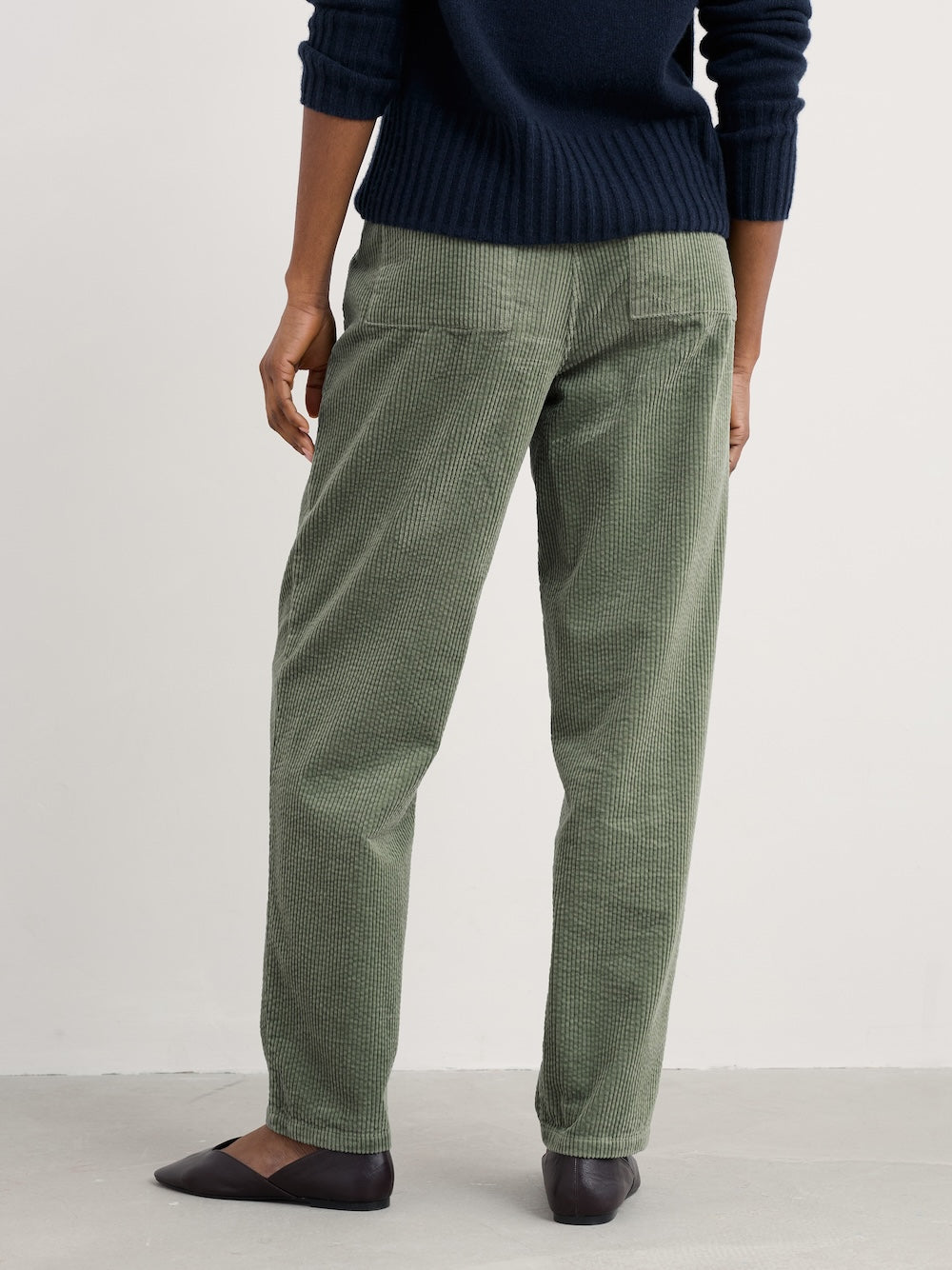 Person wearing green corduroy pants and a navy sweater on a white background