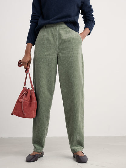 Person wearing green pants and a navy sweater, holding a red bag on a white background