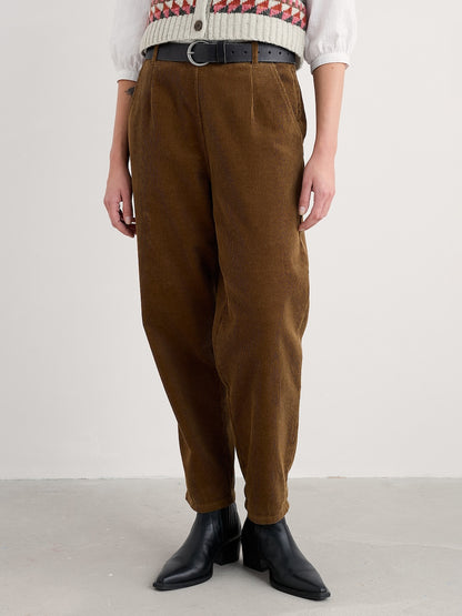 Person wearing brown corduroy pants with a white sweater and black boots on a plain background