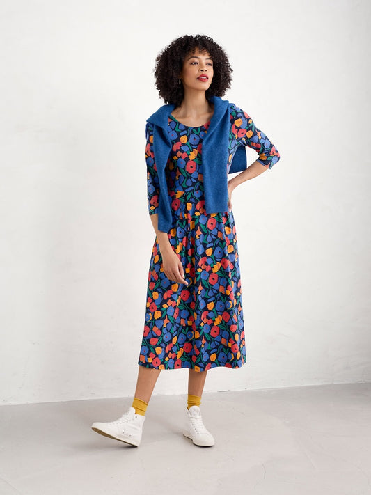 Woman wearing a colourful floral dress with a blue cardigan on a white background